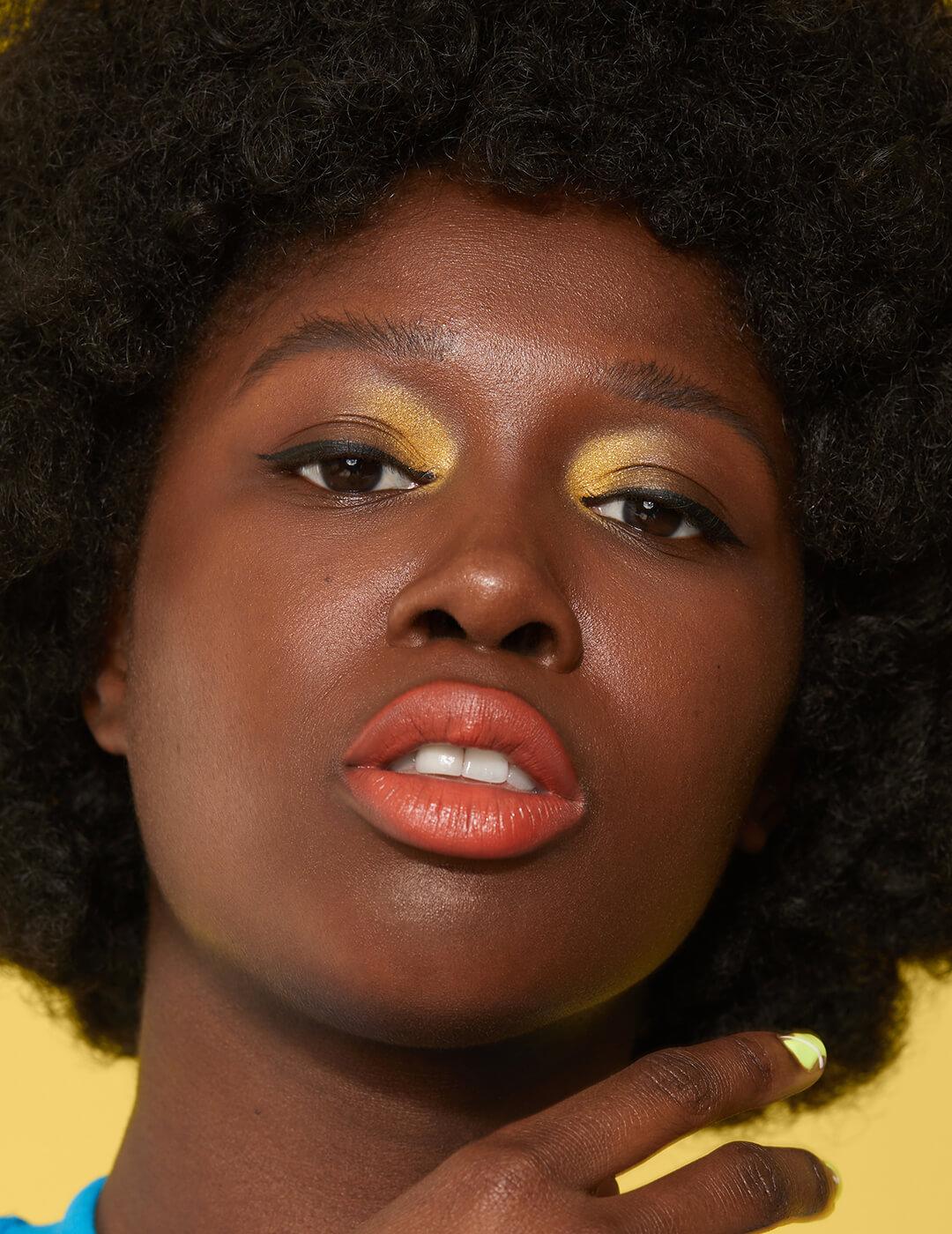Close-up of a Black model rocking gold eyeshadow and orange lips