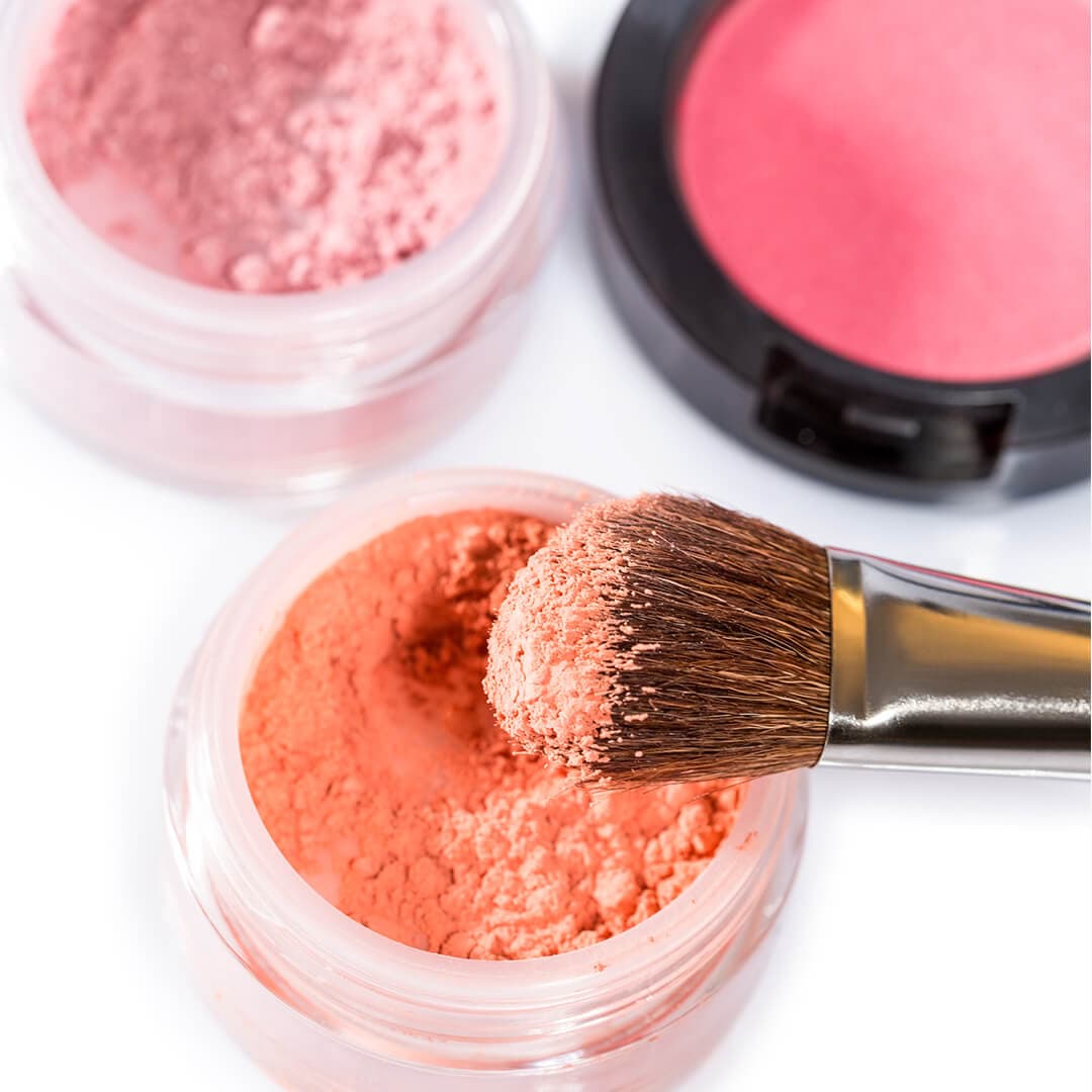 Blush brush on peach powder blush and another powder and pressed blush in the background