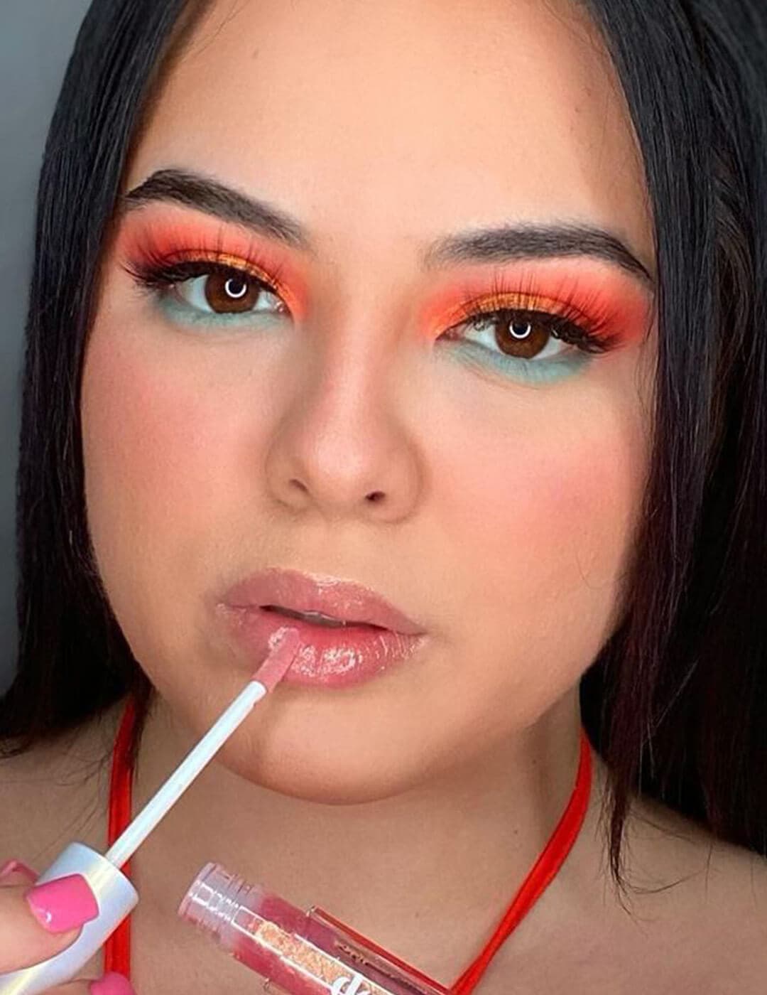 Close-up of a beautiful woman with orange and green eye makeup look applying lip gloss on her lips