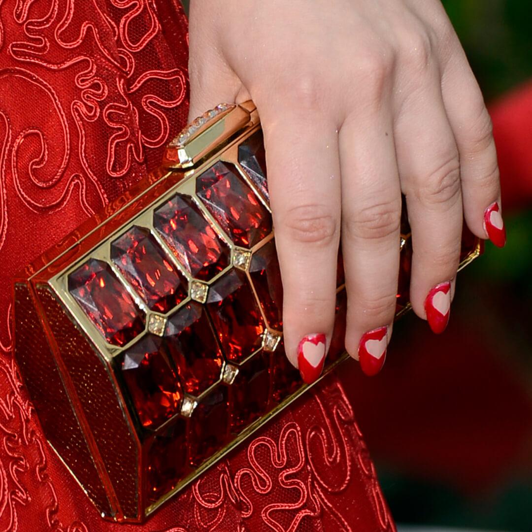 Close-up of Kaley Cuoco’s hand with negative space heart manicure holding a red-bejewelled purse