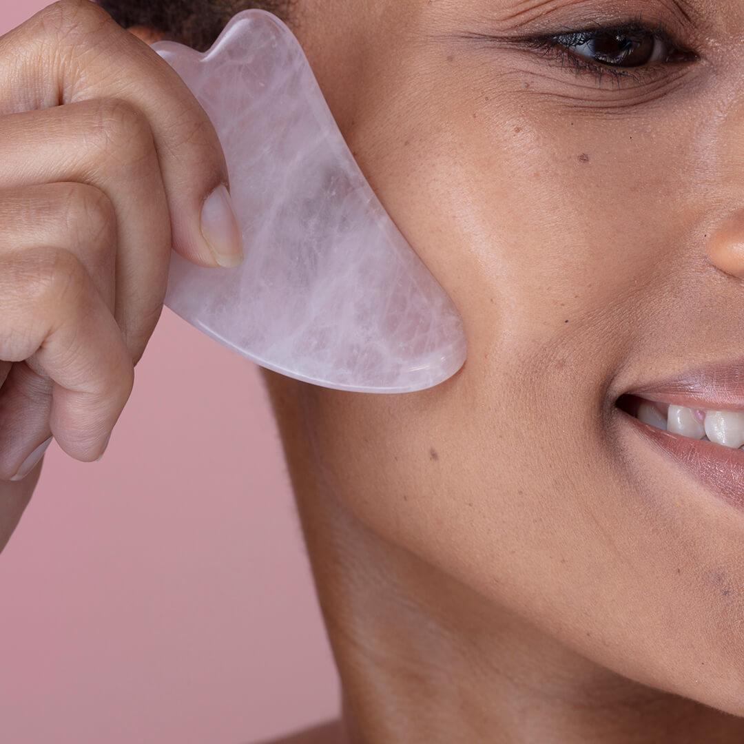 Close-up image of a woman using a pink quartz gua sha stone on her face