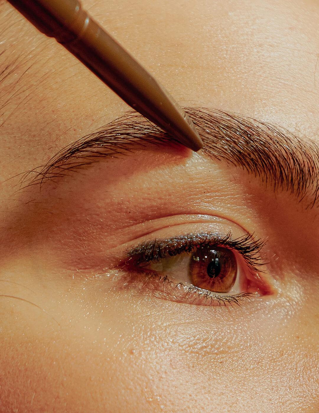 A photo of a woman's eye with a brown brow pencil on her eyebrow