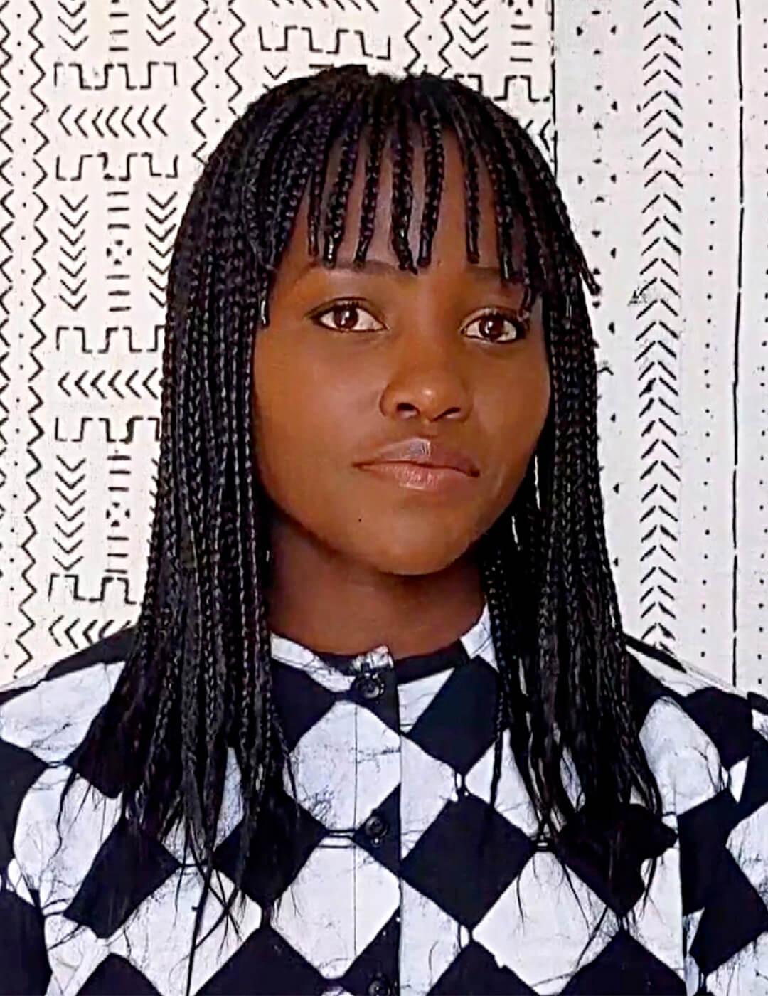 Lupita Nyong'o in a black and white geometric dress rocking a braided hairstyle with braided bangs