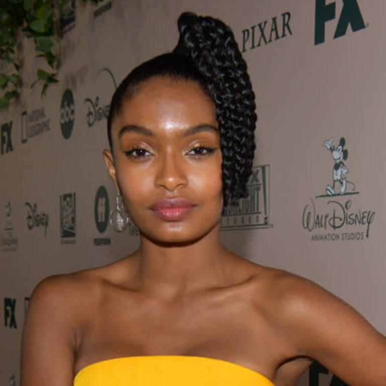 A close-up image of Yara Shahidi in a yellow tube dress rocking a braided side high pony tail hairstyle