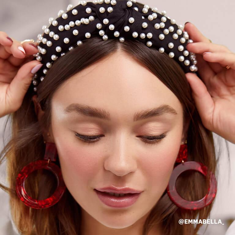 Emma Isabella Holley wearing pearl-studded headband and red statement earrings