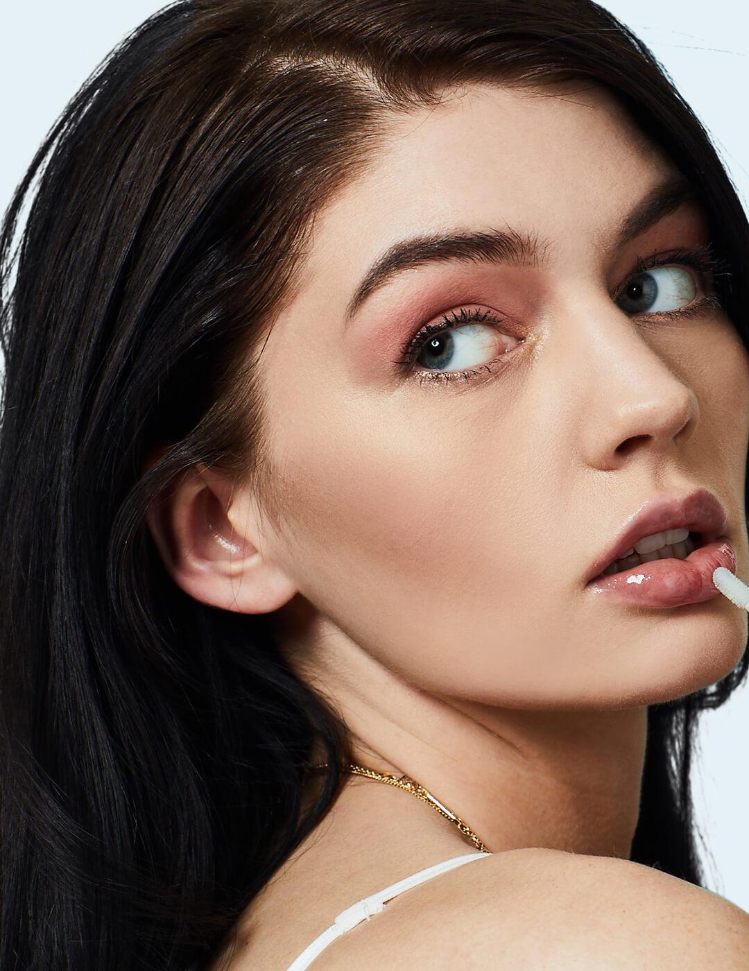 Close-up of a model applying clear lip gloss on top of her nude lip color
