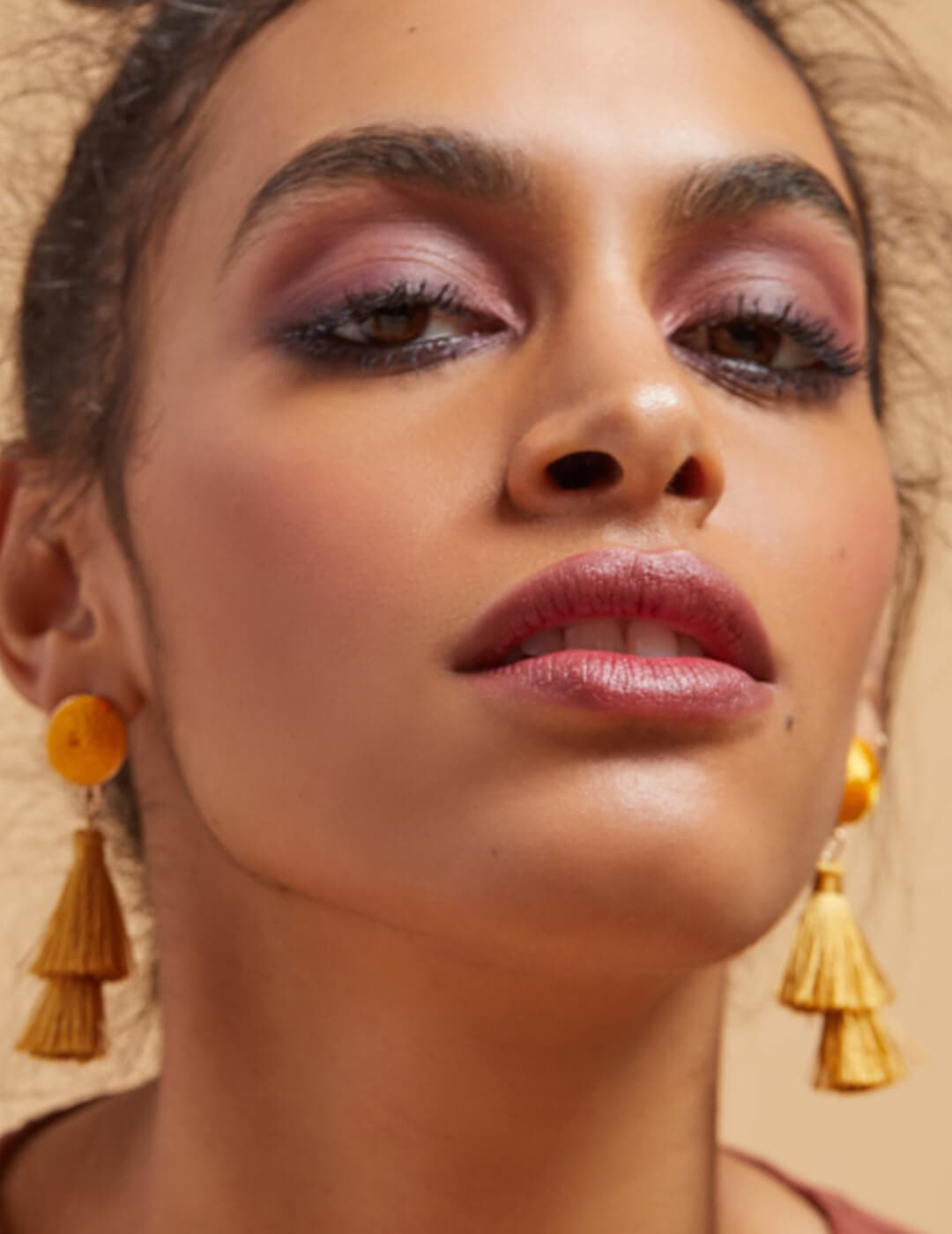 Close-up of a fierce model rocking a pink smoky eyeshadow makeup look and gold tassel earrings