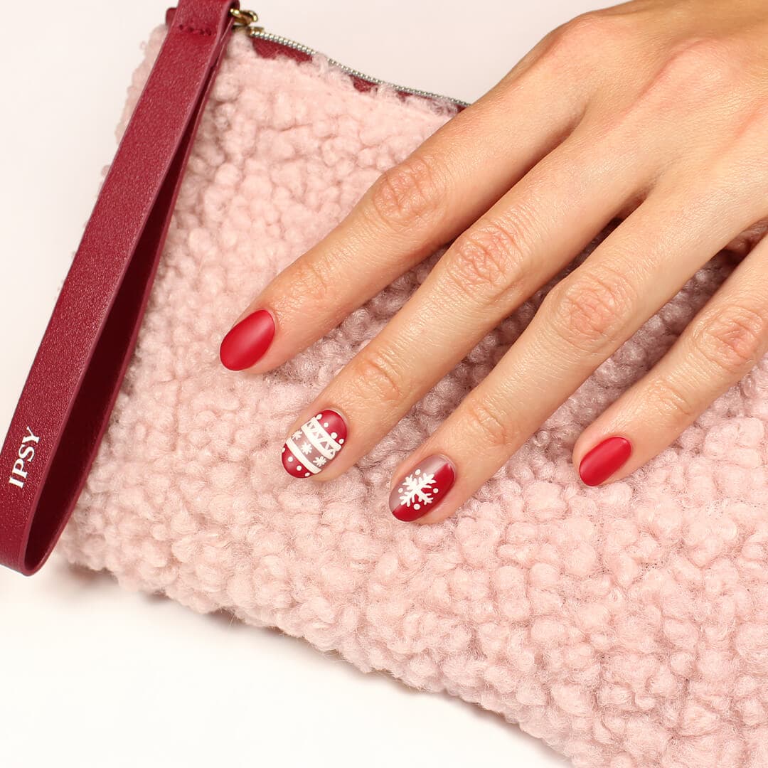 Image of a model's hand with red and white, holiday-themed nail art mani holding the December 2020 IPSY Glam Bag