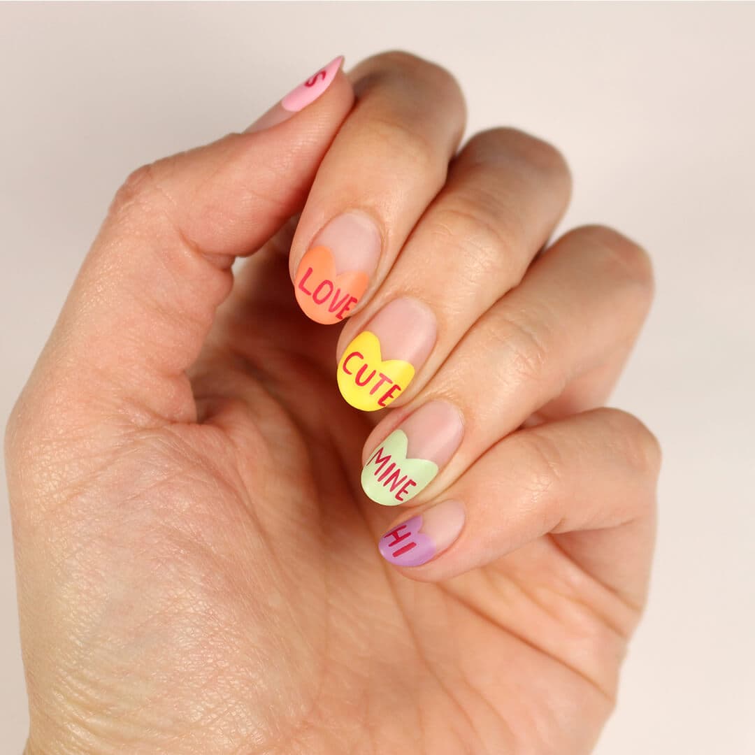Close-up image of a woman's hand with colorful heart and text nail art