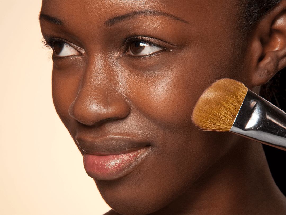 Close-up image of a Black woman putting on face makeup using a makeup brush