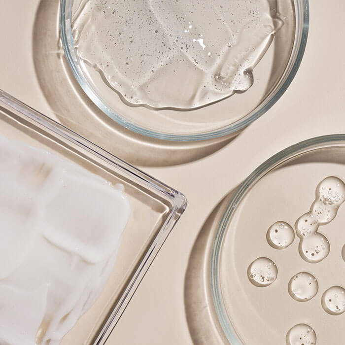 An up-close visual featuring a selection of cosmetic items such as hyaluronic acid drops, cream, and gel, displayed with smears for a detailed view
