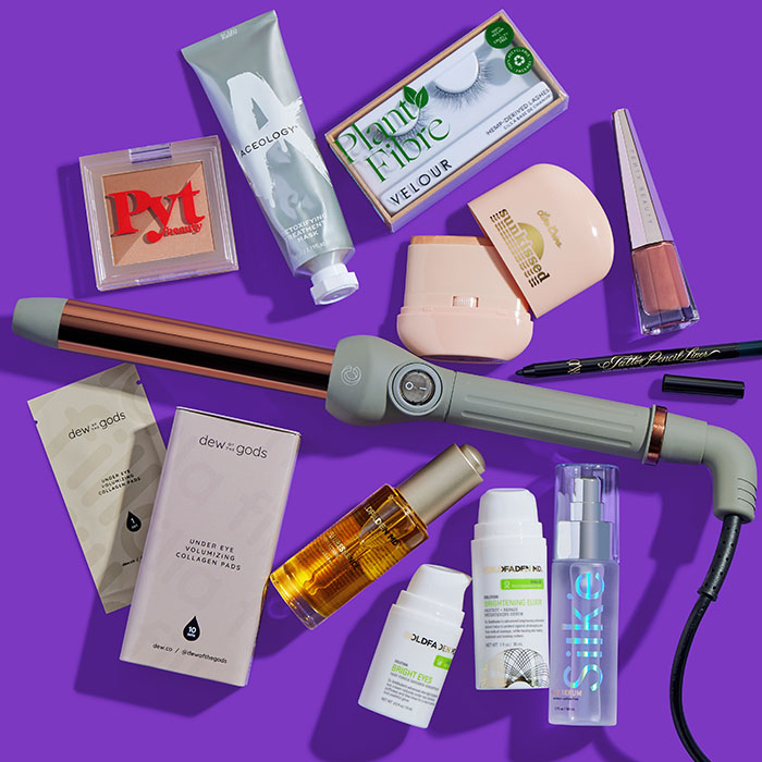 Makeup, skincare, and beauty products and tools from various brands scattered on dark purple background