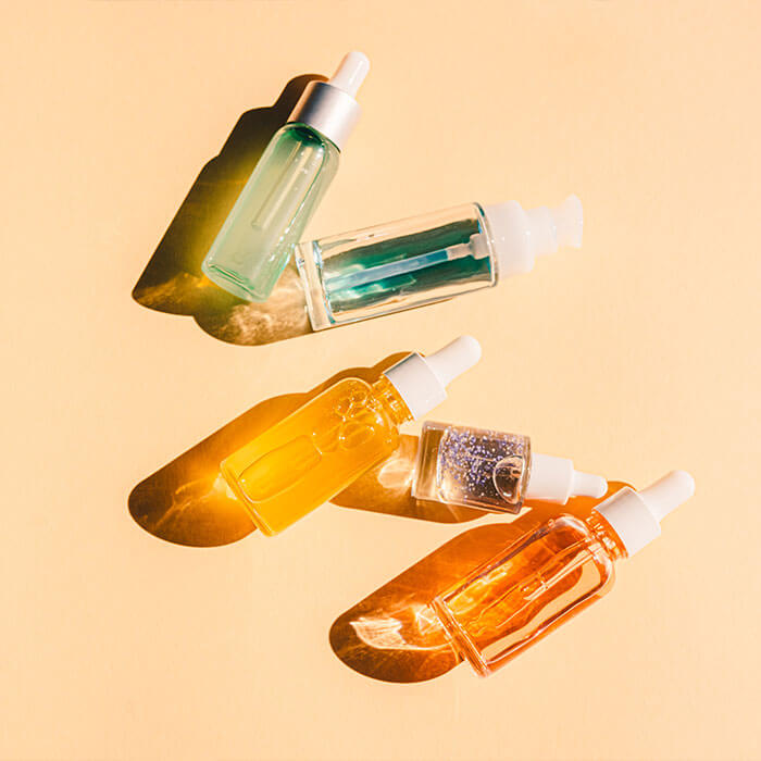 A flatlay of a variety of vibrant bottles containing liquids, serums, or gels on a peach-colored background