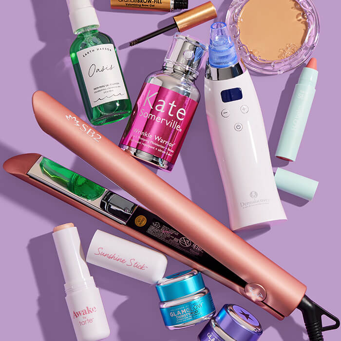 Makeup, skincare, and beauty products and tools from various brands scattered on lavender background