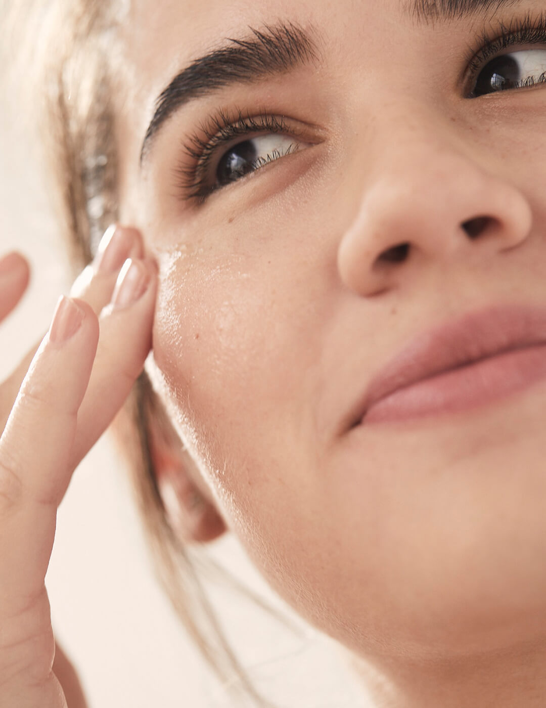 A close-up image of a model applying clear product under her eye