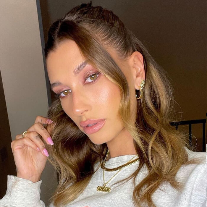 Selfie of Hailey Bieber rocking a half up ponytail hairstyle, pink monochromatic makeup look, and pink nail mani