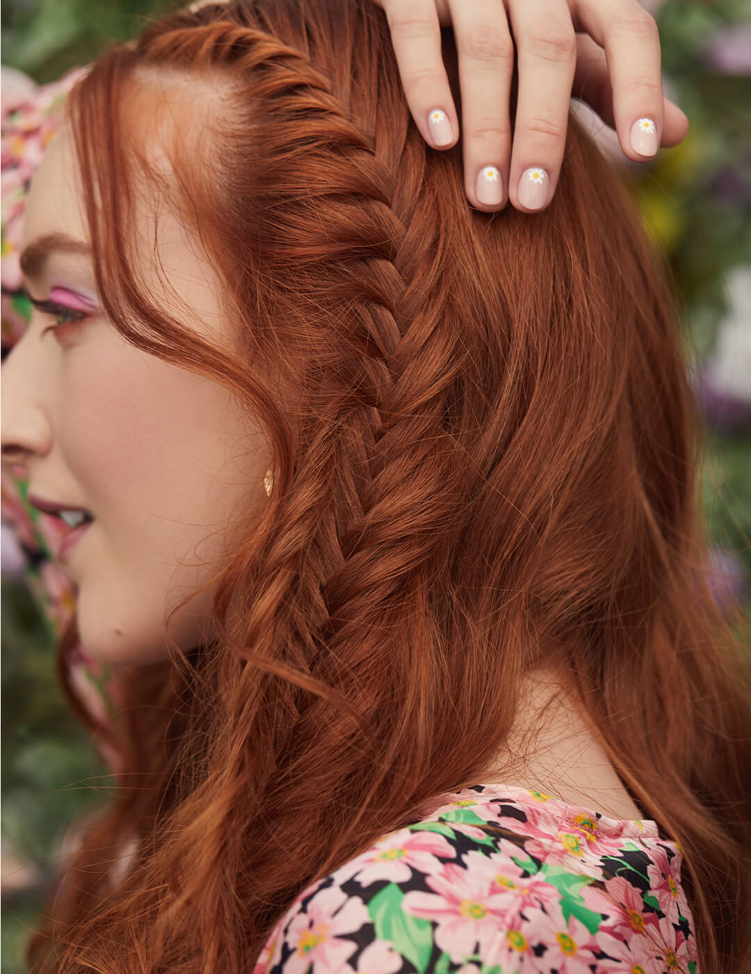 Close-up profile image of a red-haired model with side fishtail braids in a floral outfit posing