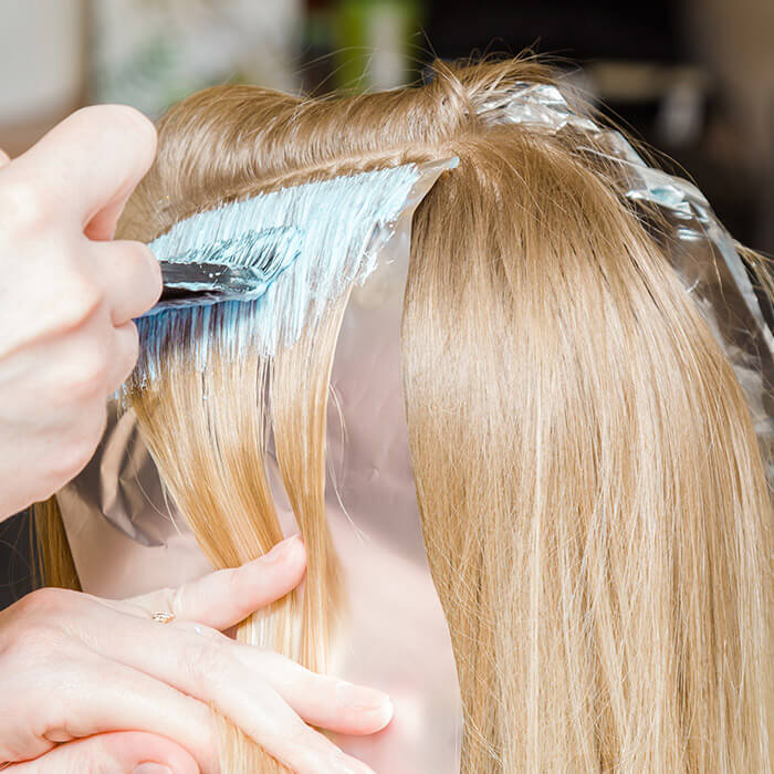 Hairdresser hands bleaching strands of blonde woman hair in beauty salon