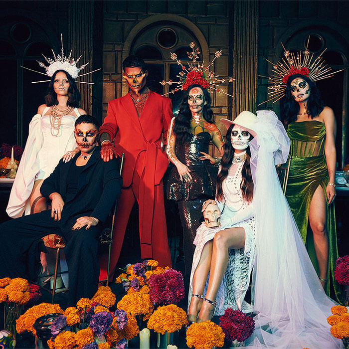 Group of six models in dia de los muertos makeup looks posing among flowers