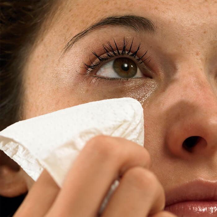 An image of a woman with stunning eyes, holding a wipe to dry her tears
