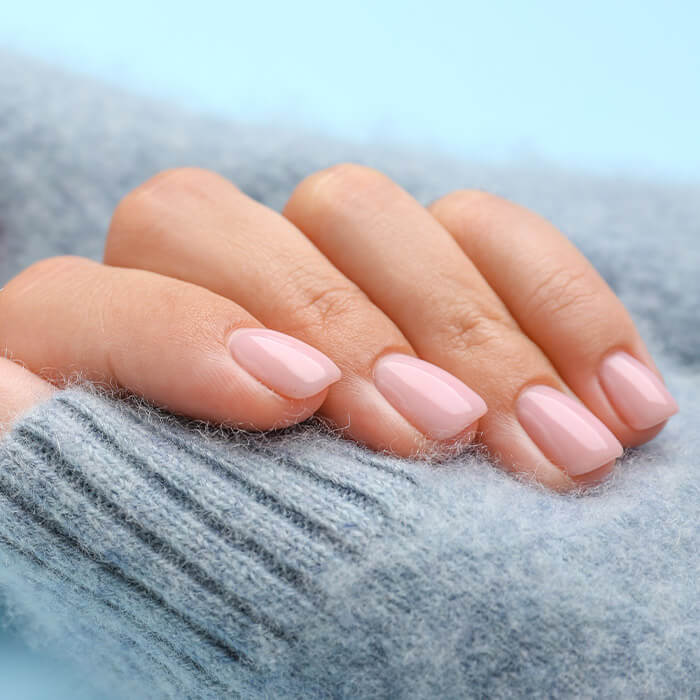 Close-up image of model's hands with nude pink mani on blue background