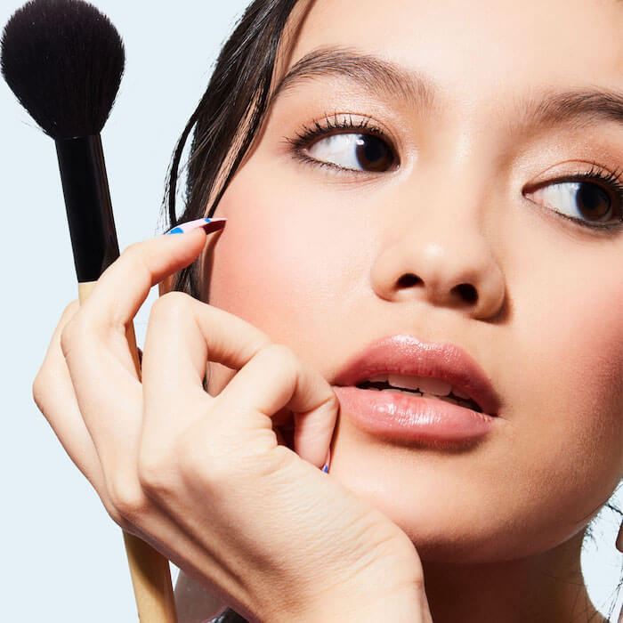 A photo of a woman with a makeup bronzer brush at her cheek