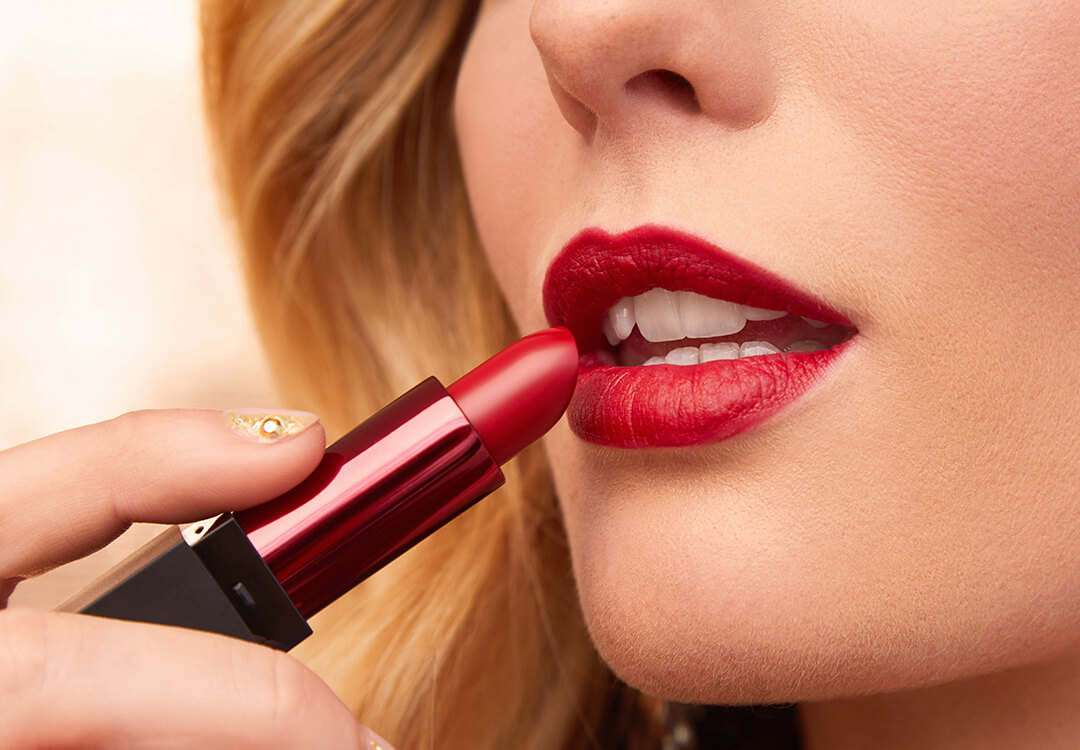 A close-up image of a model applying bold red lipstick on her lips