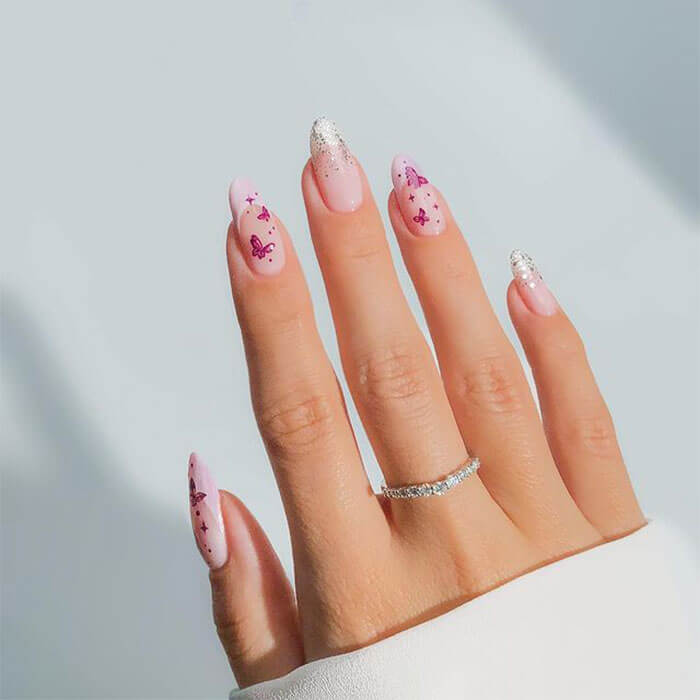 A close-up image of a woman's hand  with her nails painted in butterfly motif in soft pink hues