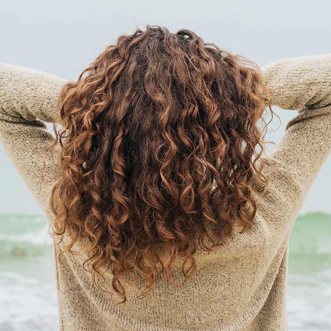 A photo of a woman showing her defined curly hair on a beach background