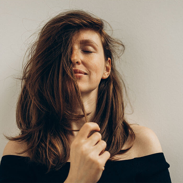 A woman with long, voluminous, healthy hair enjoys the wonderful smell of her hair with her eyes closed