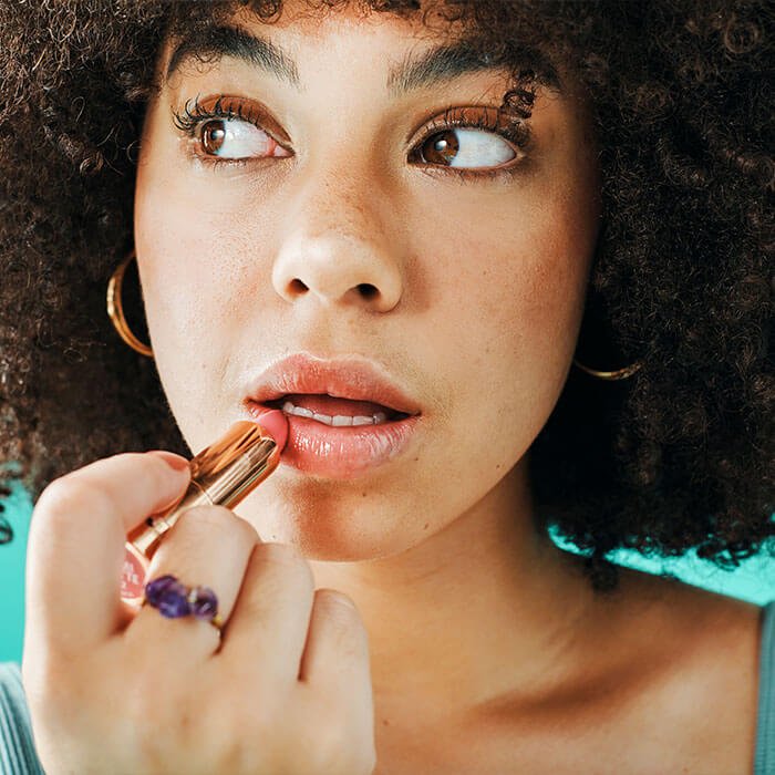 A close-up image of a curly-haired girl applying lipstick