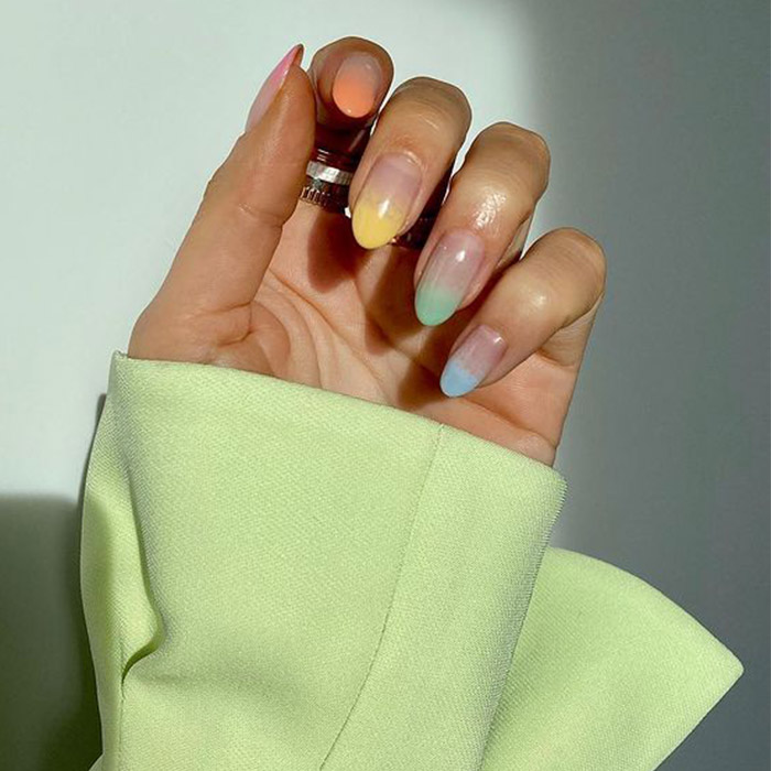 A closeup of a model's hand with a faded pastel rainbow nail polish