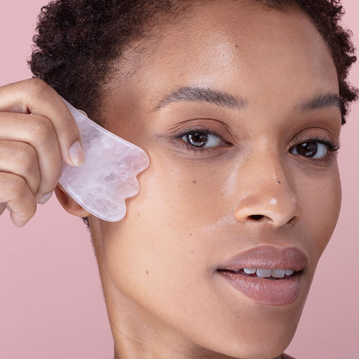 Close-up image of a woman using a pink quartz gua sha stone on her face