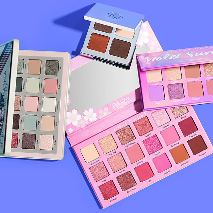 Colorful eyeshadow palettes from various brands on blue background