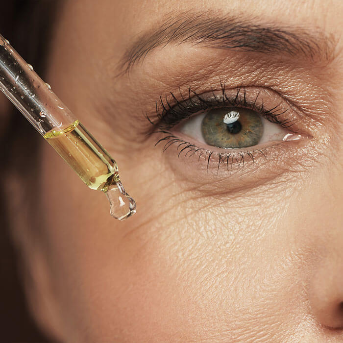 An image capturing the close-up detail of an elderly woman's eye with an eyedrop serum dropper