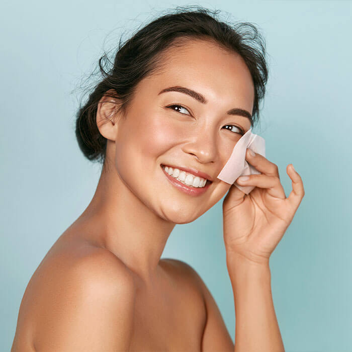 A woman with a fresh and clean appearance is seen blotting excess oil from her face with blotting paper, demonstrating a practical approach to controlling oily skin