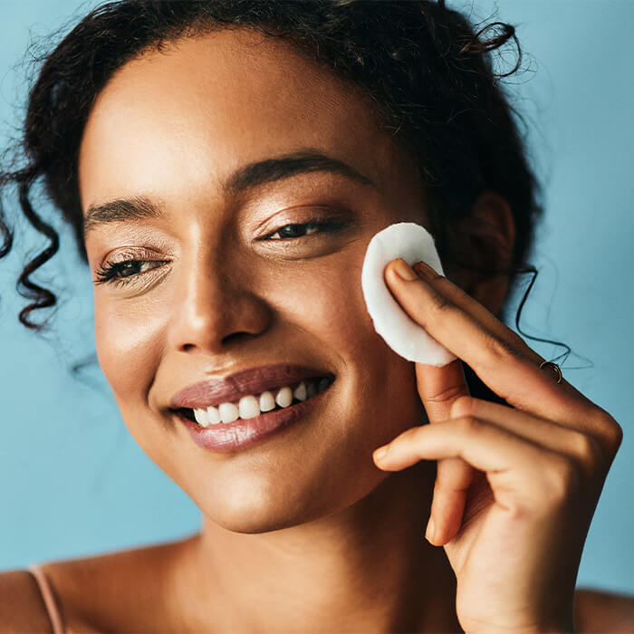 Smiling woman applying toner with a round cotton pad against blue background
