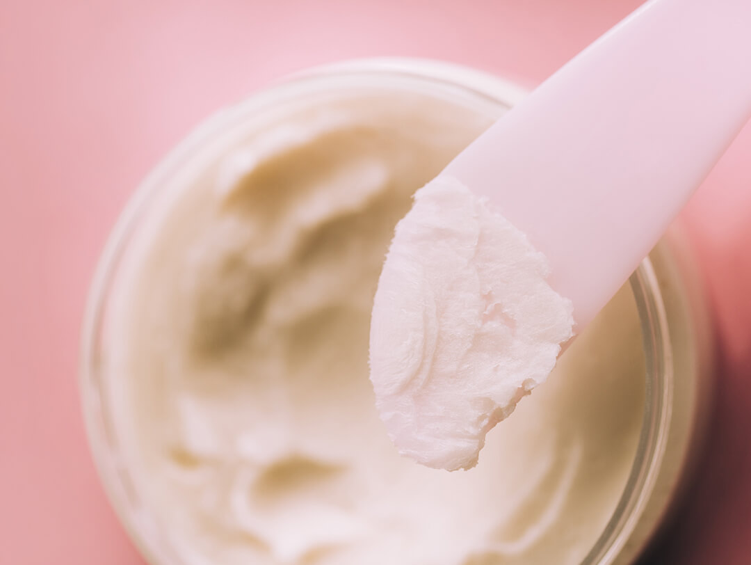 A jar of hardened coconut oil with pink spatula against pink background