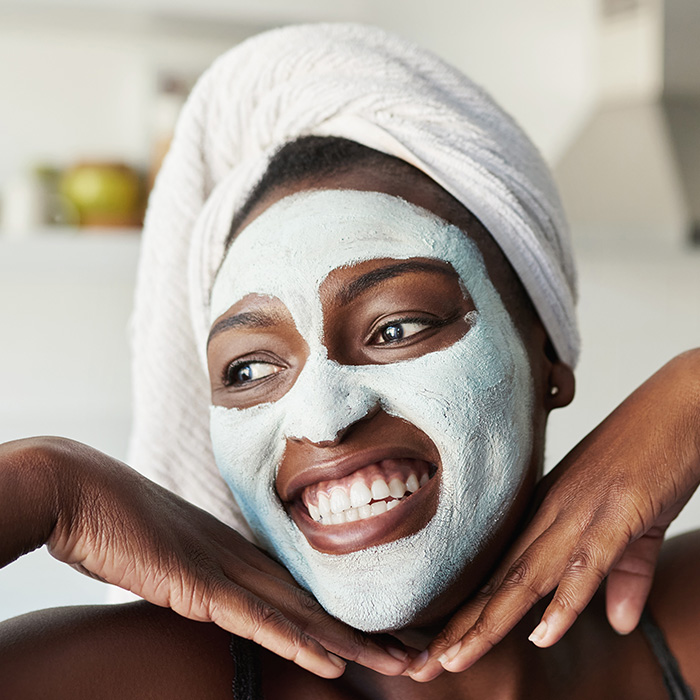 An image of a smiling woman with a mud mask on her face