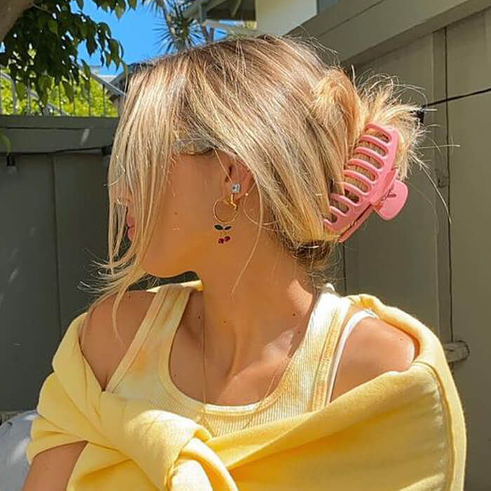 Close-up of a woman with pink clamp on her hair and yellow outfit posing in her backyard