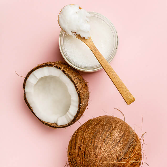 Coconut half, jar of coconut oil, and wooden spoon on pink background