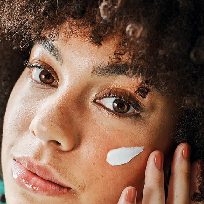 Closeup photo of a woman applying cream on her cheek