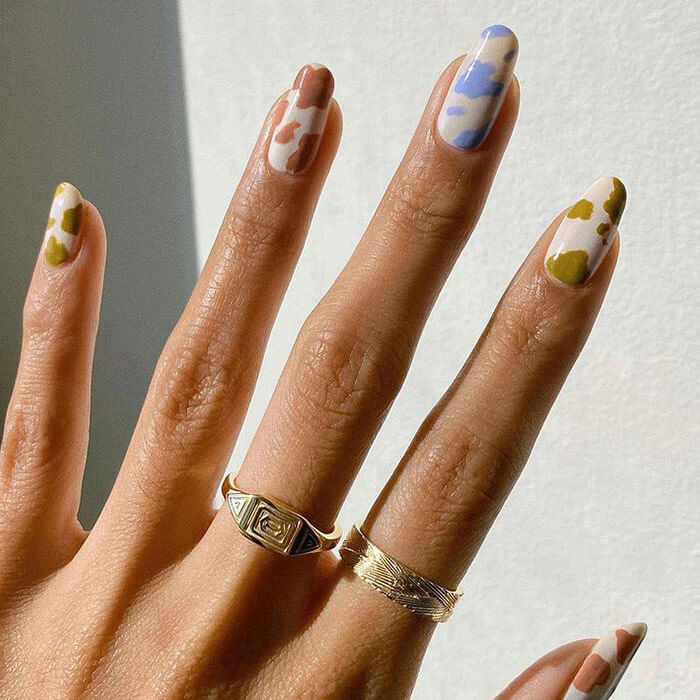 A closeup photo of a model's hand with pastel color cow print nail art