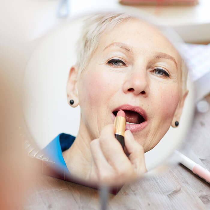 Mature woman applying lipstick while looking at a mirror