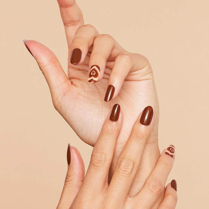 Close-up of model's hands with dark brown nail art and nail polish