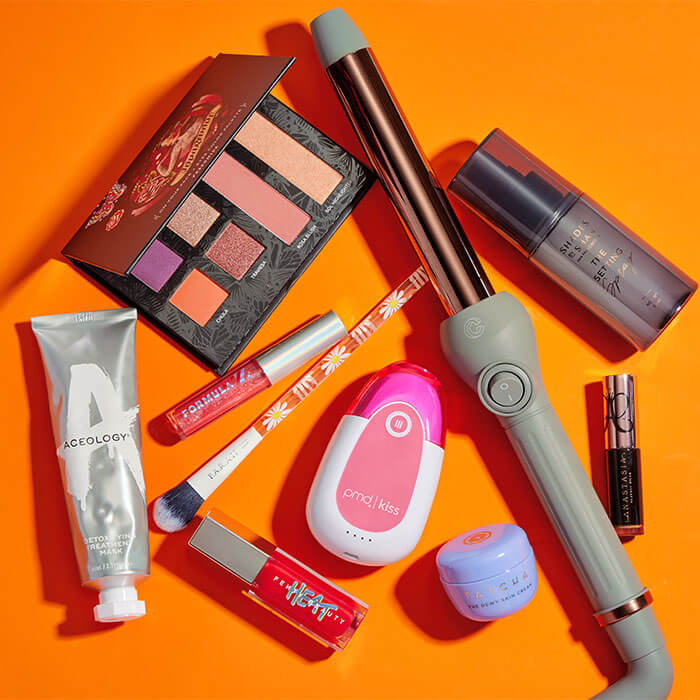 Beauty and makeup products and tools from various brands scattered on dark orange background