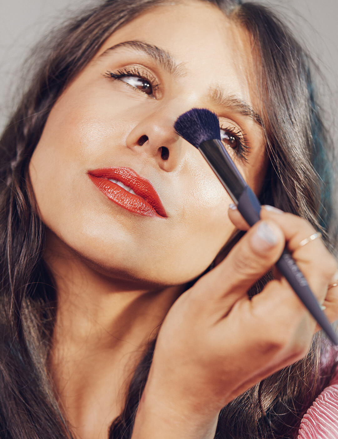 An image of a model touching her nose with a makeup brush