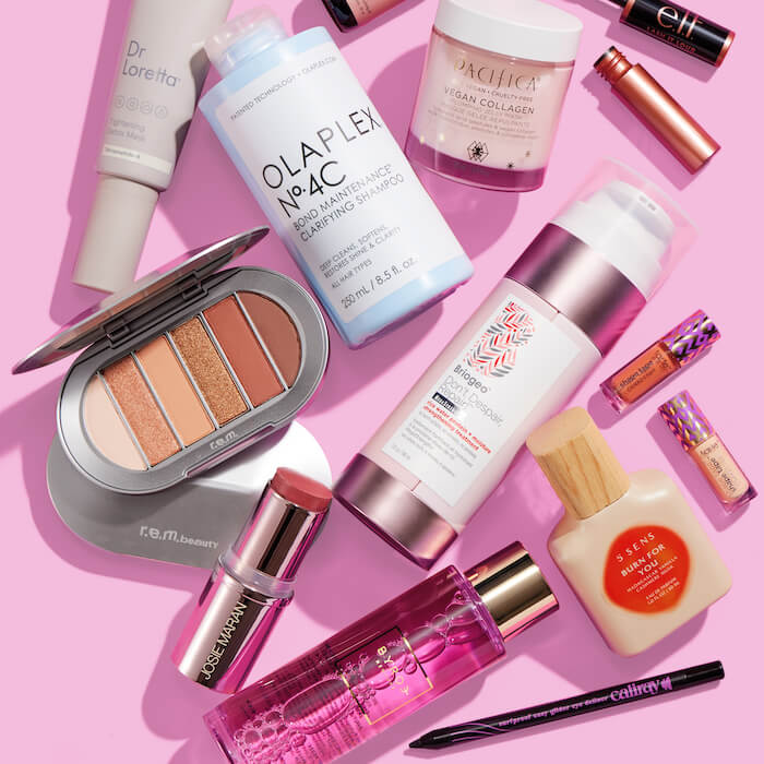 Beauty and makeup products from various brands scattered on pink background
