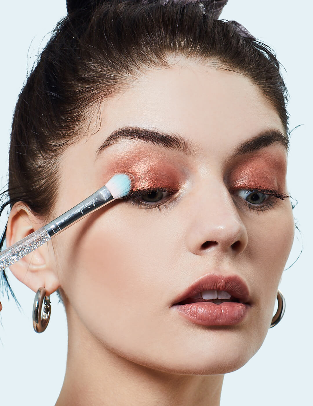 Close-up of a model applying shimmery nude eyeshadow on her eyelids using a small brush