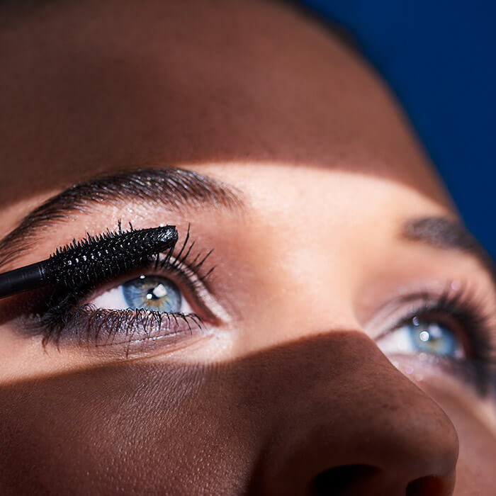 Close-up of a woman's blue eyes and applying mascara